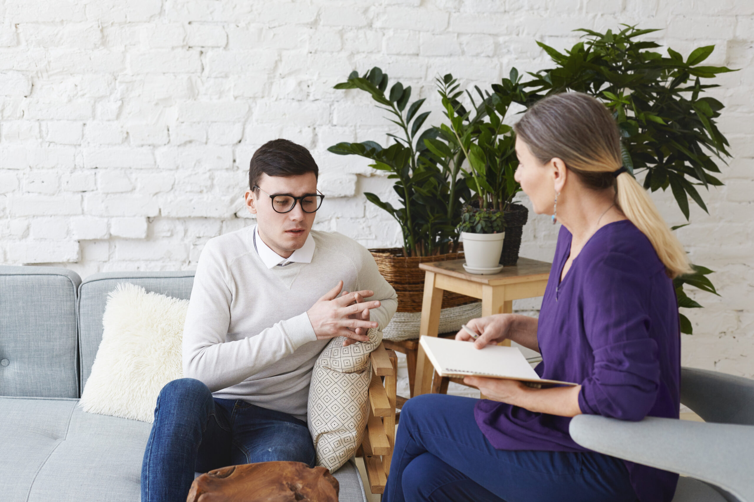 A young man in glasses talking through his struggles while his therapist listens and takes notes