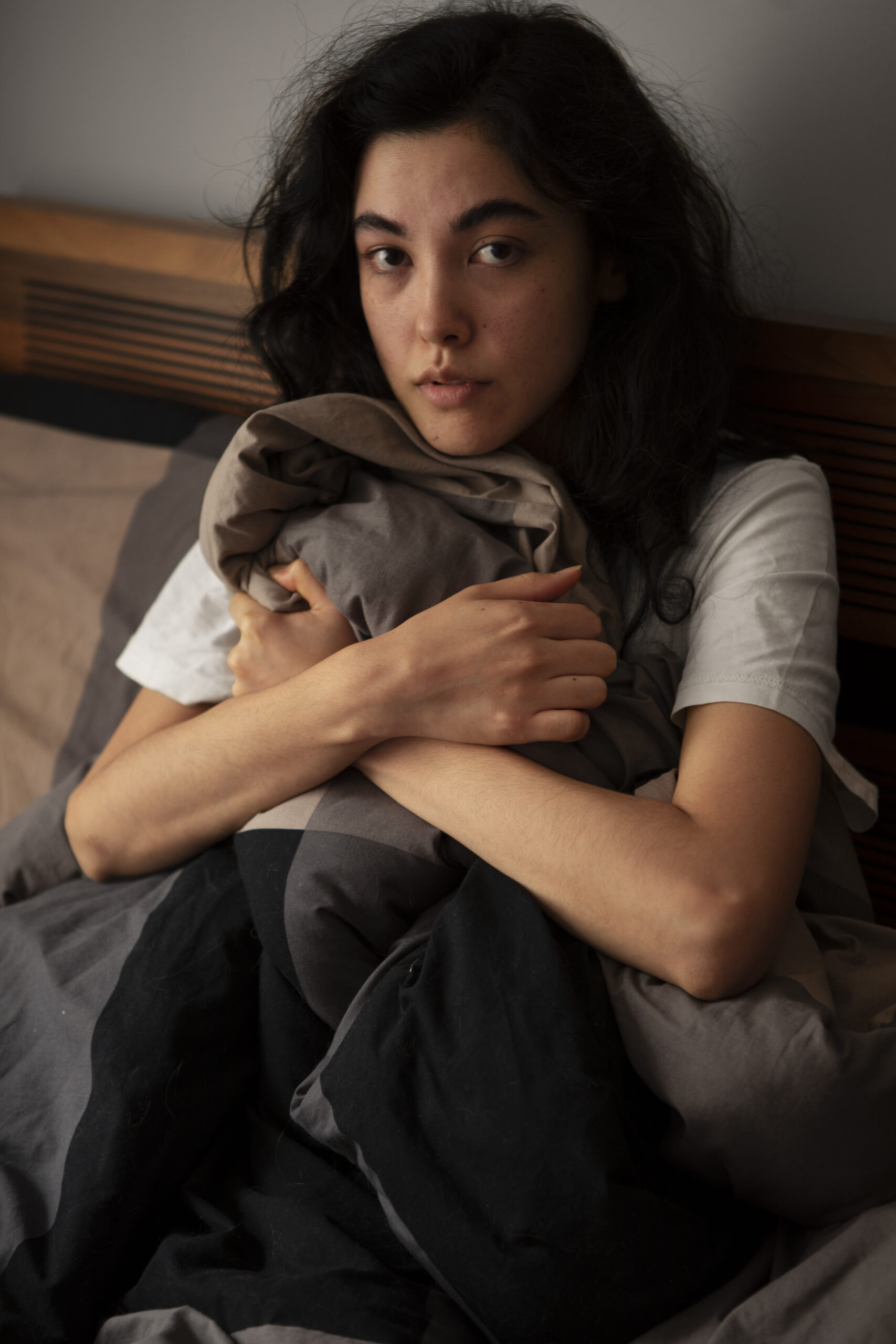 A woman sitting wrapped in a blanket, looking tired and worn down despite holding it together